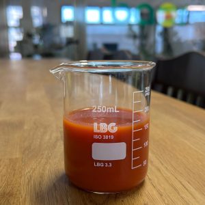 Organic tomato juice NFC sample in a lab beaker, deep red color, Mediterranean origin