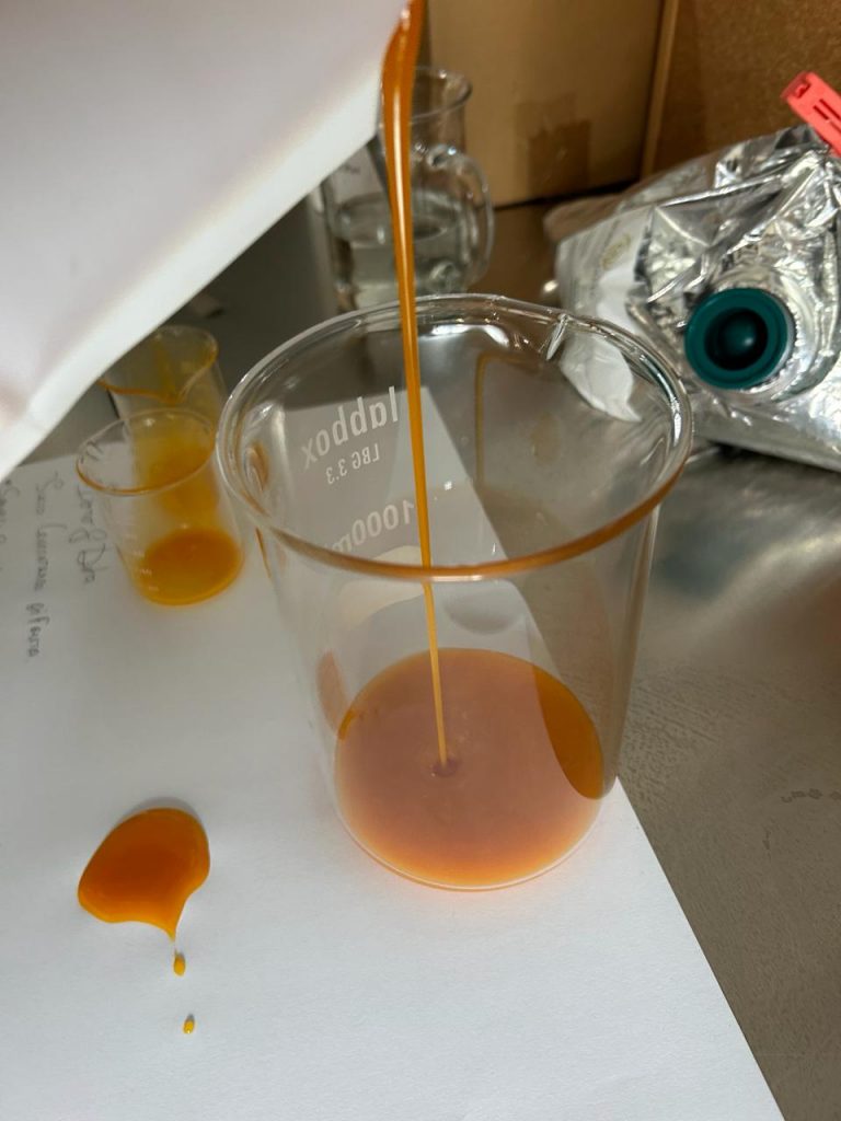 Tropical multifruit juice concentrate flowing into laboratory beaker, showing viscosity and texture during industrial formulation.