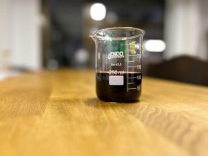 Organic blueberry vinegar sample in laboratory beaker showing dark color and liquid consistency for industrial quality control